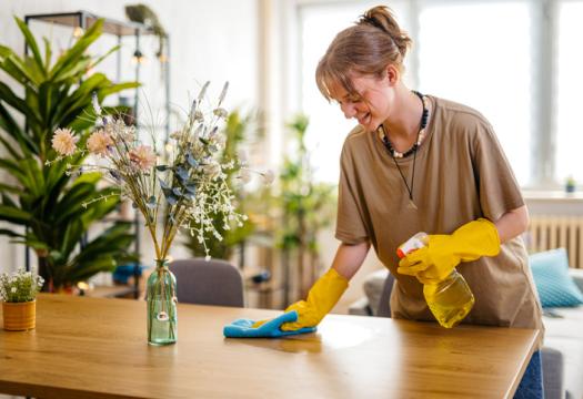Young smiling woman wiping the dining table surface using a cloth and a spray bottle | Merry Maids