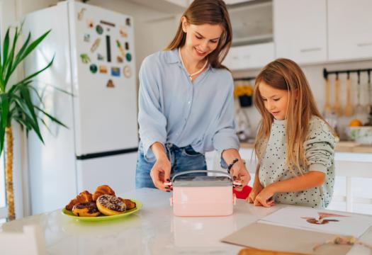 Cheerful woman closes the lunch box and prepares her daughter for school | Merry Maids