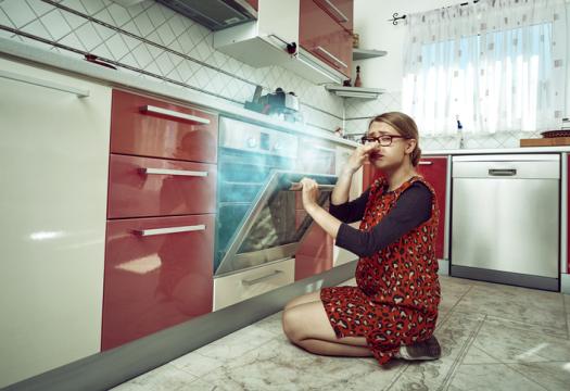 Young woman inside her kitchen opening the stove, burning food inside it, negative expression | Merry Maids