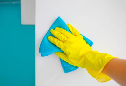 Female hand in yellow rubber gloves wipes a modern white kitchen with a microfiber cloth. | Merry Maids